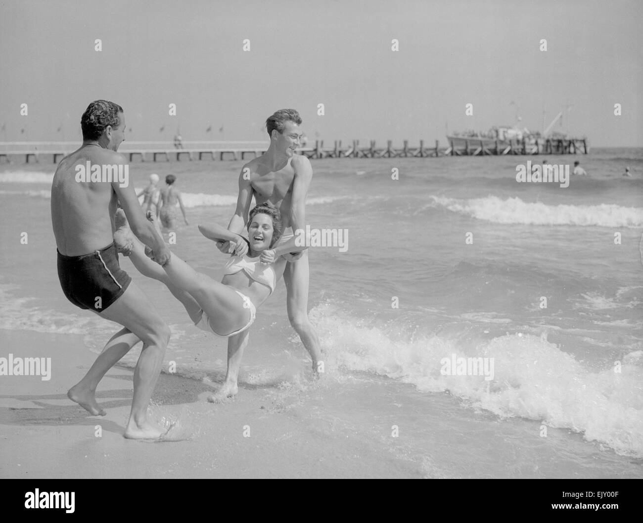 Due uomini di gettare una giovane donna in mare sulla spiaggia di Bournemouth. Decimo Aust 1952 Foto Stock