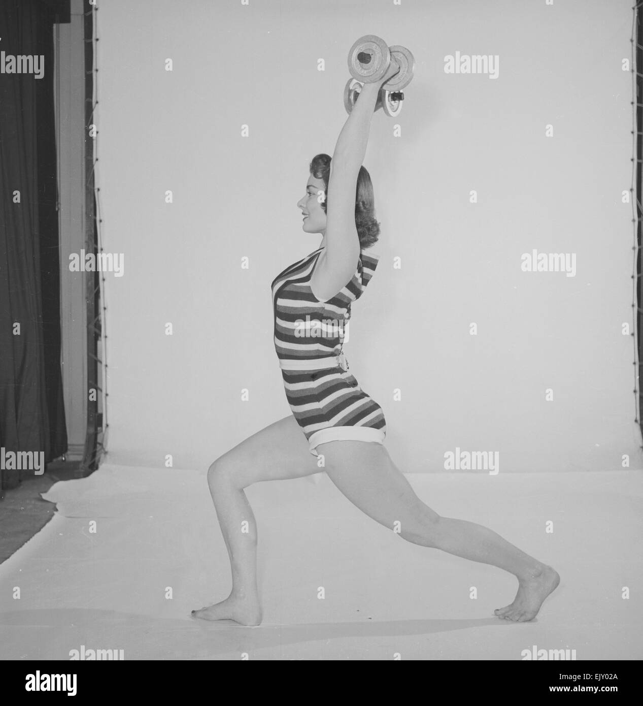 Sveglia ' mantenere giovane e bellissima e caratteristica, donna che indossa un pezzo la balneazione costune esercizio con pesi circa 1958 Foto Stock