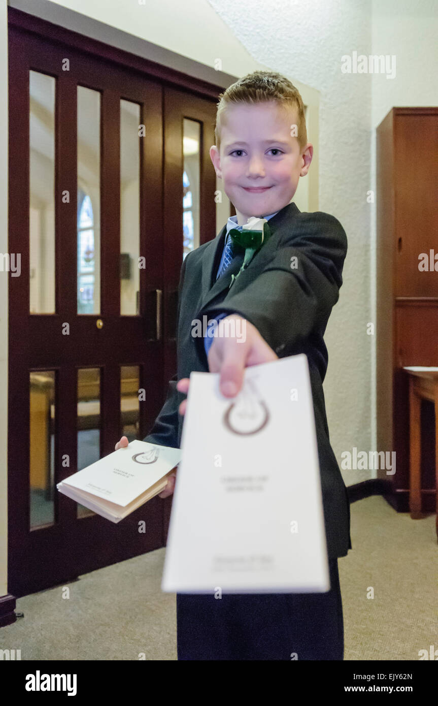 Un ragazzo giovane usher mani gli ordini di servizio per i rapporti che arrivano a un matrimonio in una chiesa Foto Stock