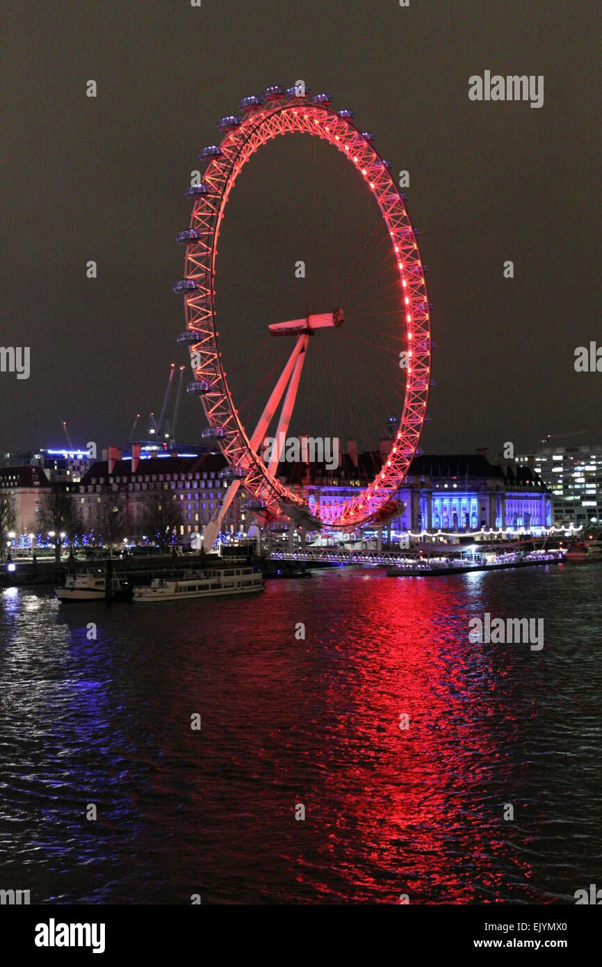 Londra England Regno Unito. Il 2 aprile 2015. Dopo il tramonto sulla Southbank London Eye è illuminato con le luci rosse della attuale sponsor Coca-Cola. Come si vede dal Giubileo ponte pedonale attraverso il fiume Tamigi. Foto Stock