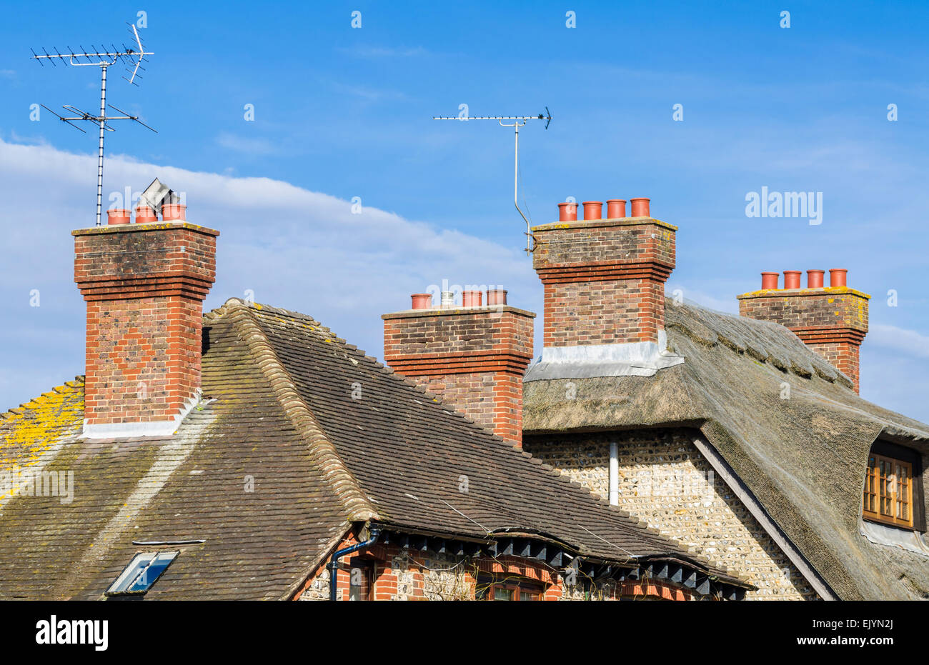 Mattone rosso ciminiere sul tetto in paglia ed i tetti in Inghilterra, Regno Unito. Foto Stock