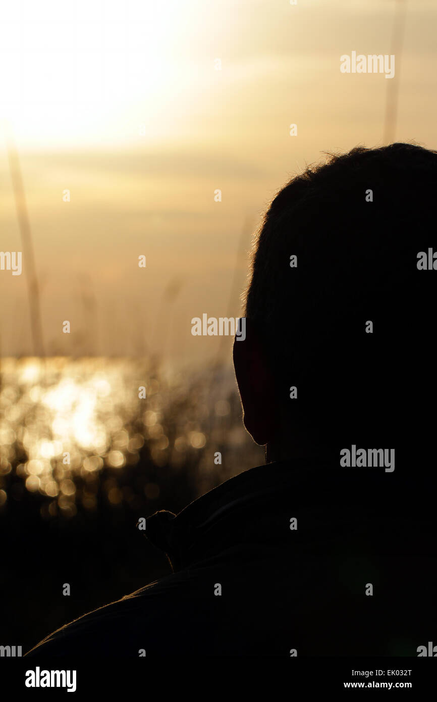 Uomo maturo torna Silhouette al tramonto in un lago Foto Stock