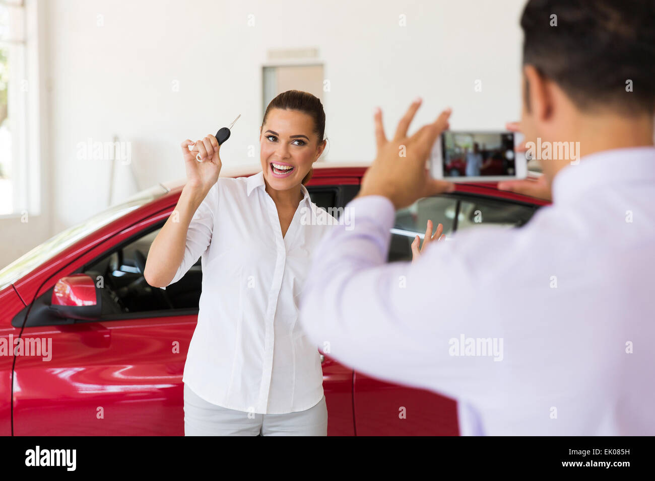 Venditore di scattare una foto del Excited donna accanto alla sua nuova vettura in showroom Foto Stock