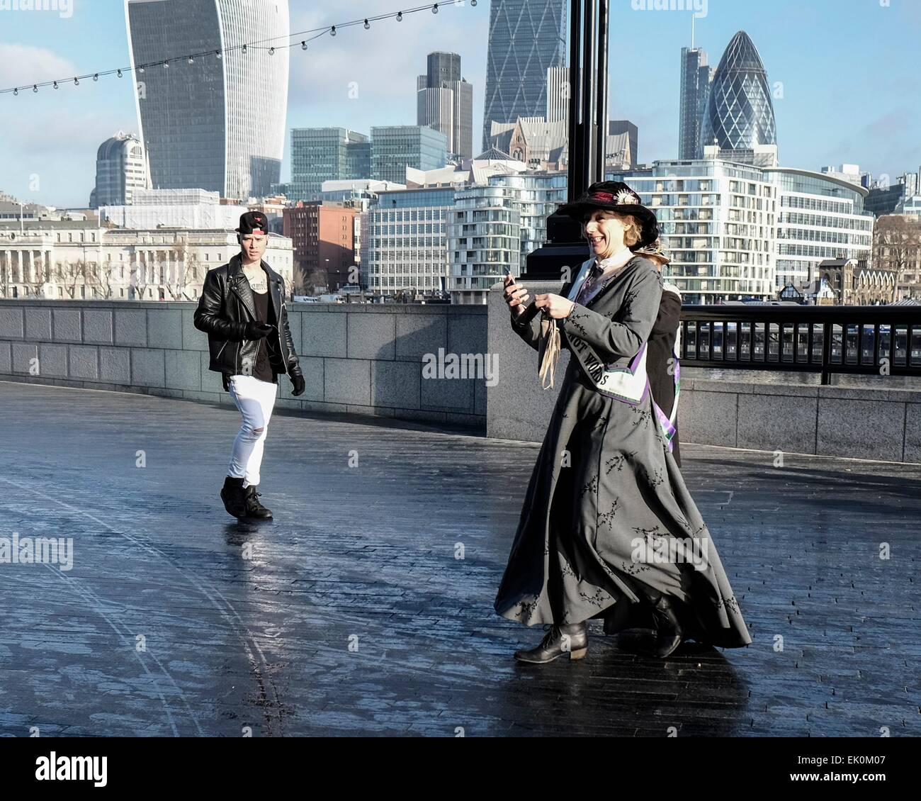Un giovane uomo in abito moderno guarda una donna nel periodo suffragette vestito come egli cammina passato Foto Stock