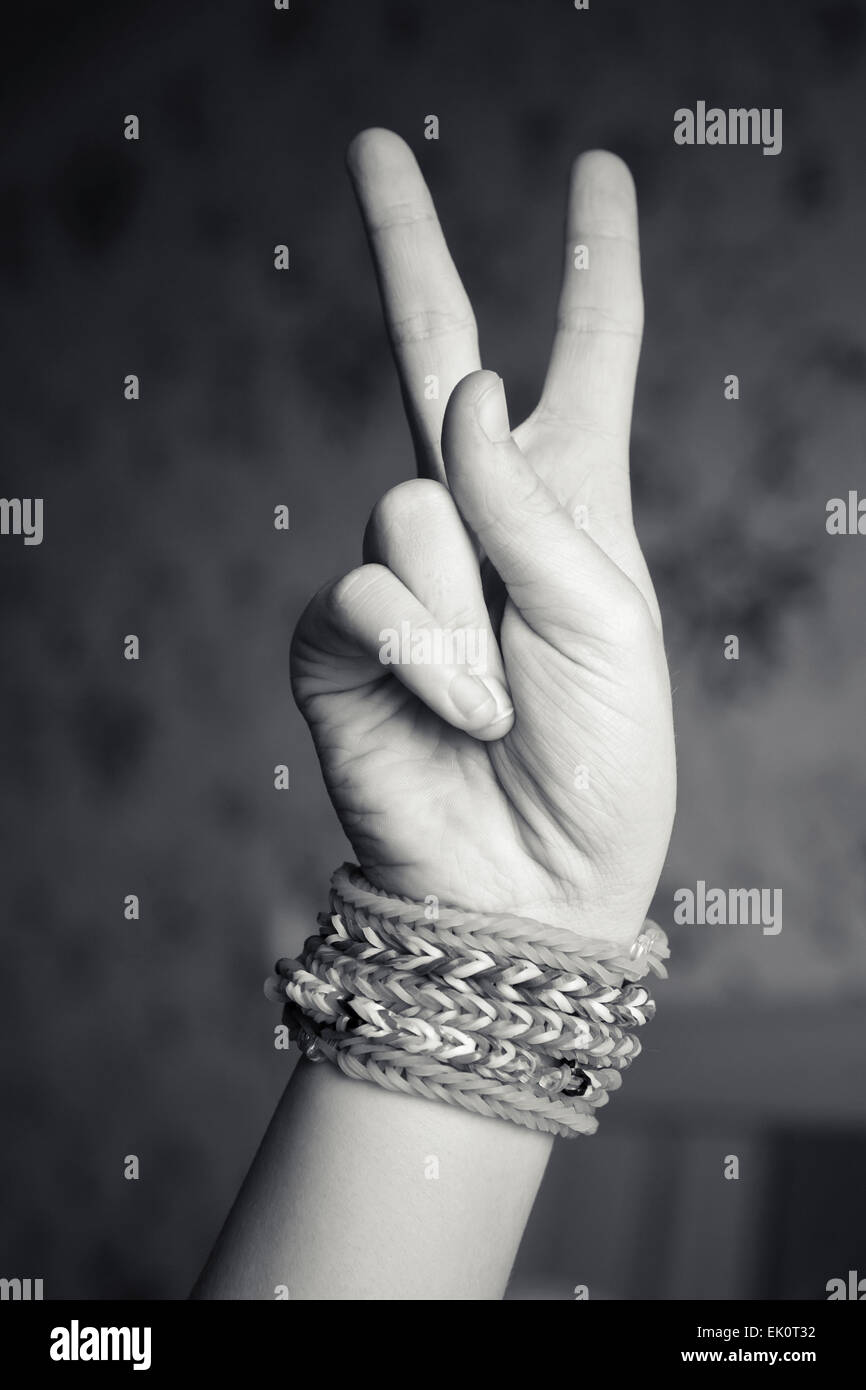 La mano del bambino che mostra segno di vittoria con gomma rainbow telaio braccialetti al polso, adolescenti alla moda accessori di moda. Vi monocromatica Foto Stock