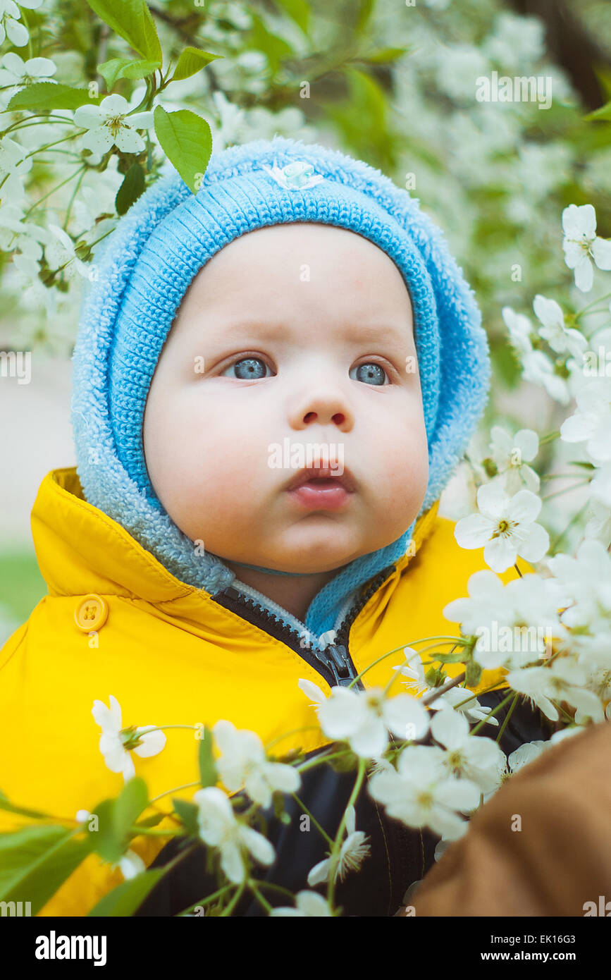 Carino piccolo bambino in blu hat su molla alberi in fiore sfondo. bel ragazzo con gli occhi blu. parenting amore o concetto. Foto Stock