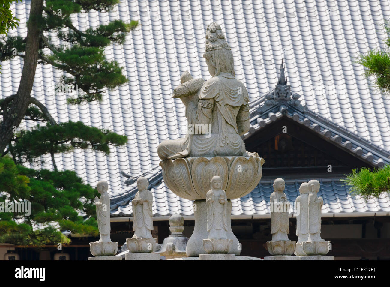 La Statua della Dea della Misericordia con alberi di pino e tetto di tegole del santuario di Itsukushima , Miyajima, Giappone Foto Stock