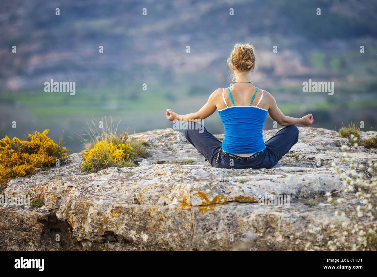 Giovane donna seduta su una roccia in posizione asana Foto Stock