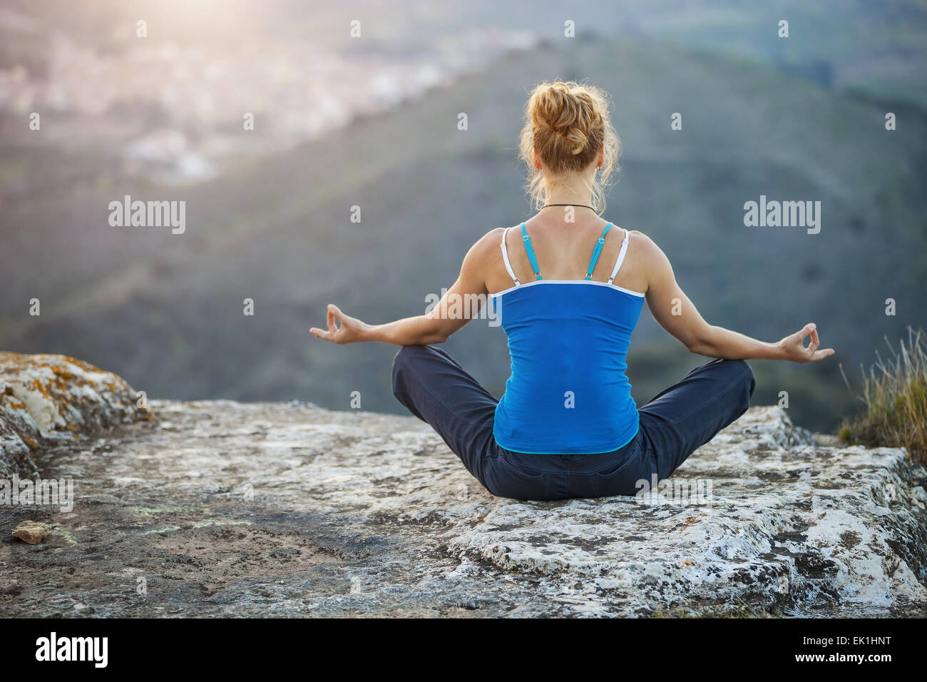 Giovane donna seduta su una roccia e godersi la vista della valle. La ragazza si siede nella posizione asana. Foto Stock