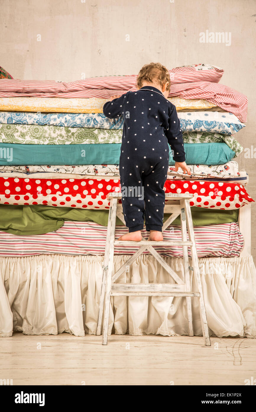 Il bambino si arrampica sul letto con un sacco di trapunte - La principessa sul pisello. Foto Stock