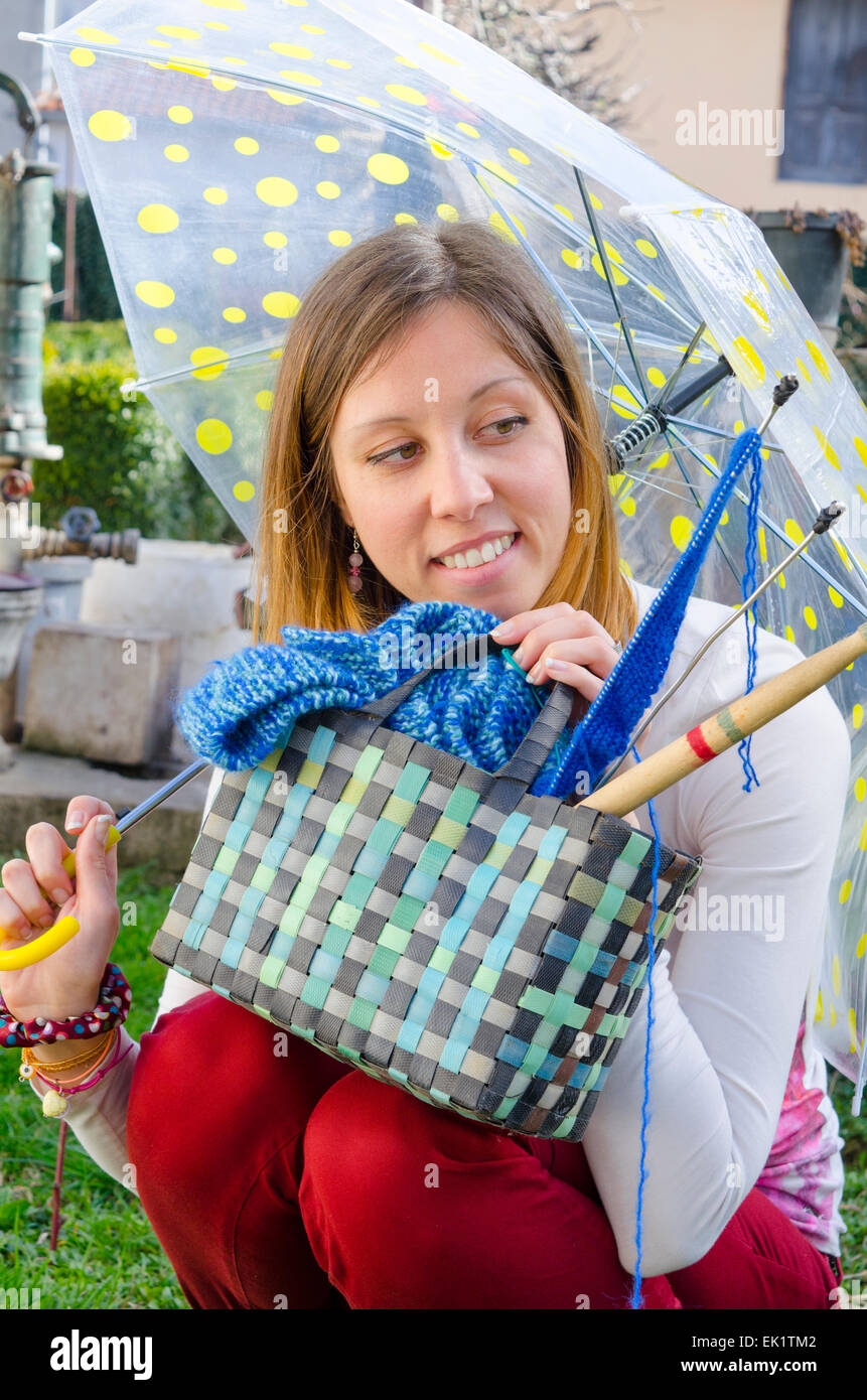 Ragazza sorridente sotto ombrellone colorato con i suoi strumenti di lavorazione a maglia Foto Stock