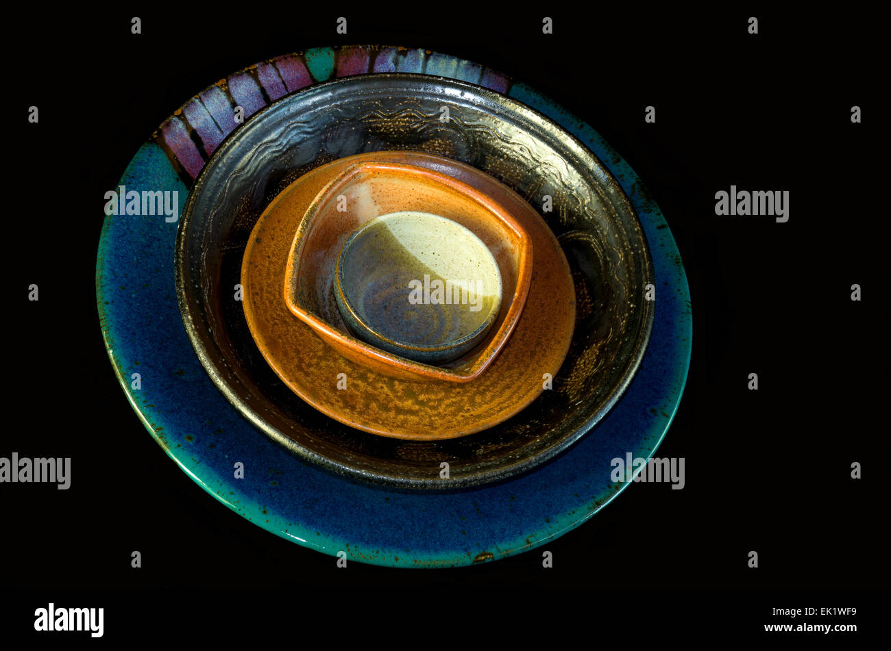Colorata a mano di ceramica ciotole piattino e servire piatto impilati all'interno di ciascun altro e isolata contro backgro nero Foto Stock