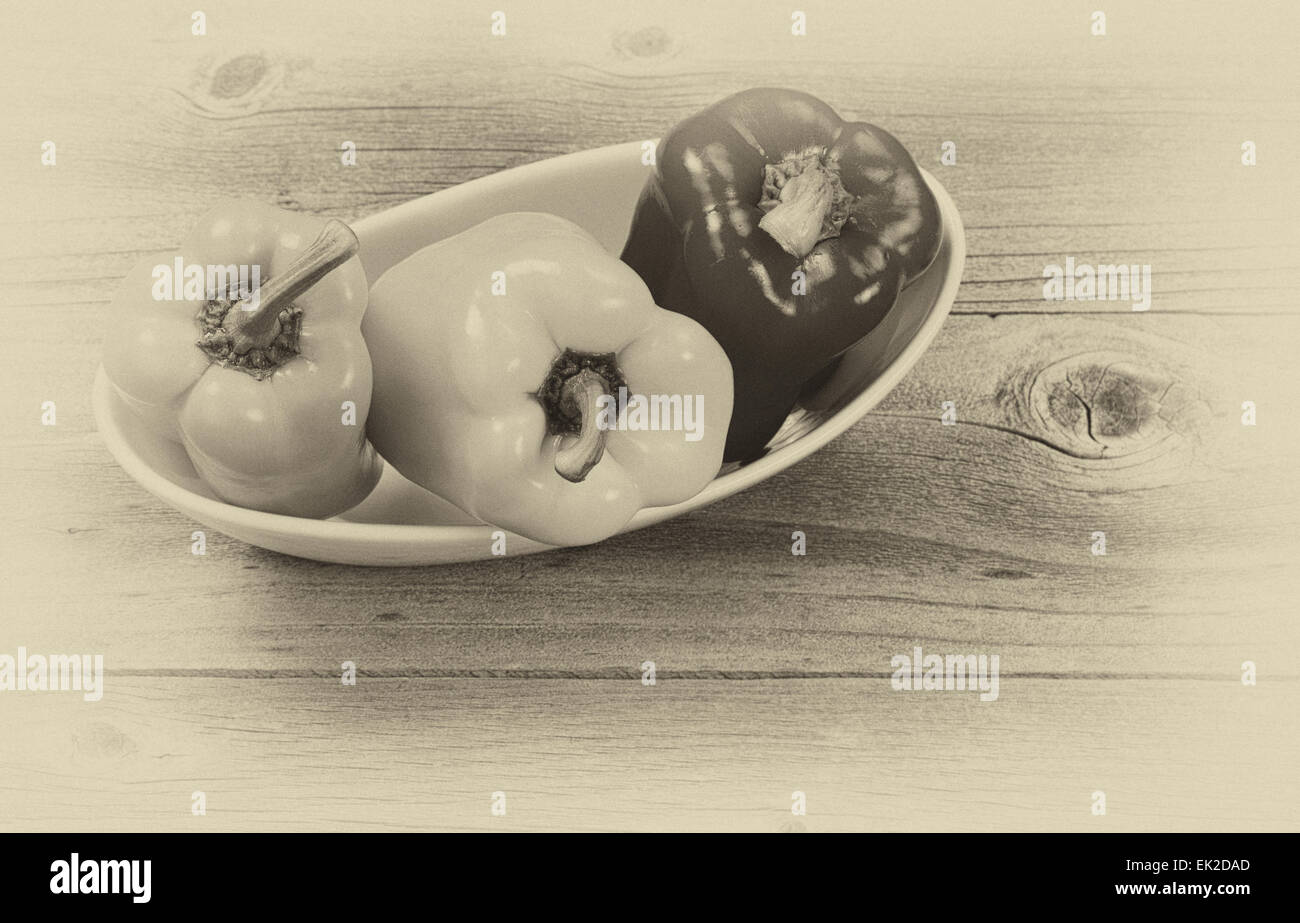 Concetto di vintage di tre nuovi i peperoni in bianco ciotola di legno invecchiato Foto Stock