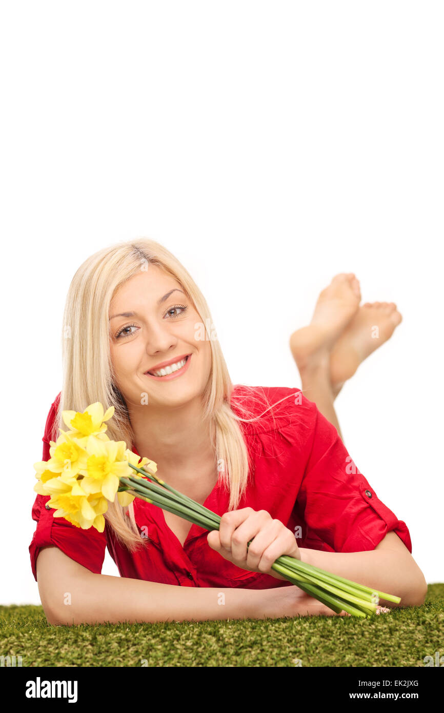 Colpo verticale di una giovane donna bionda tenendo un mazzo di tulipani gialli e giacente su di una superficie di erba Foto Stock