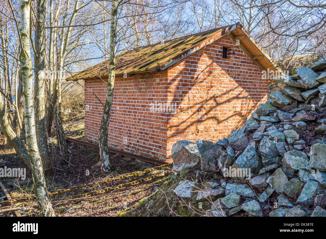 Piccolo edificio di mattoni rossi nella foresta vicino al mucchio di pietre. La Betulla gli alberi crescono vicino a casa. Foto Stock