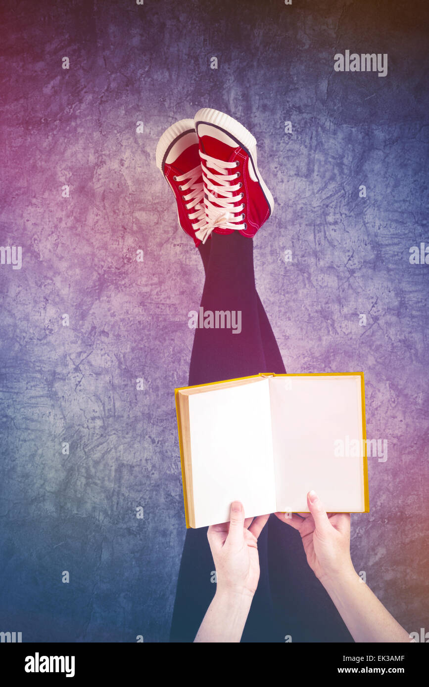 Giovane donna la lettura di Pulp Fiction libro con i suoi piedi sollevati in aria, Pagine vuote come copia di spazio. Foto Stock