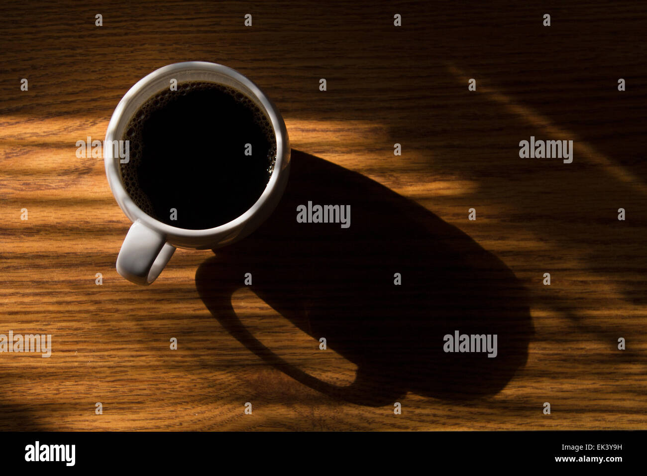Una nuova tazza di caffè si siede su una scrivania in sole mattutino. Foto Stock