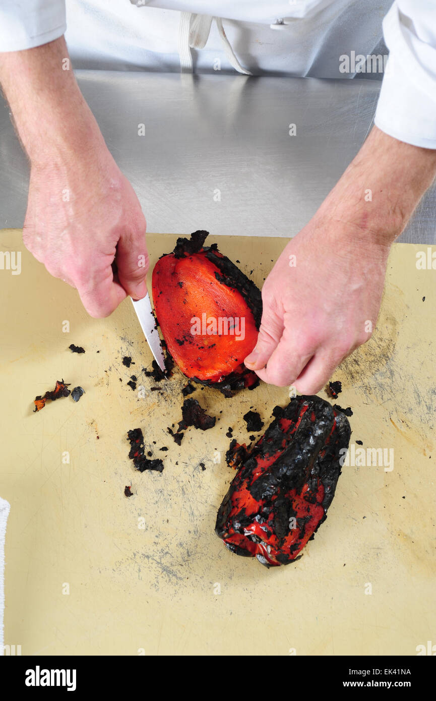 Un chef utilizza un coltello per raschiare la carbonizzazione la pelle esterna di un peperone rosso per fare una salsa Foto Stock