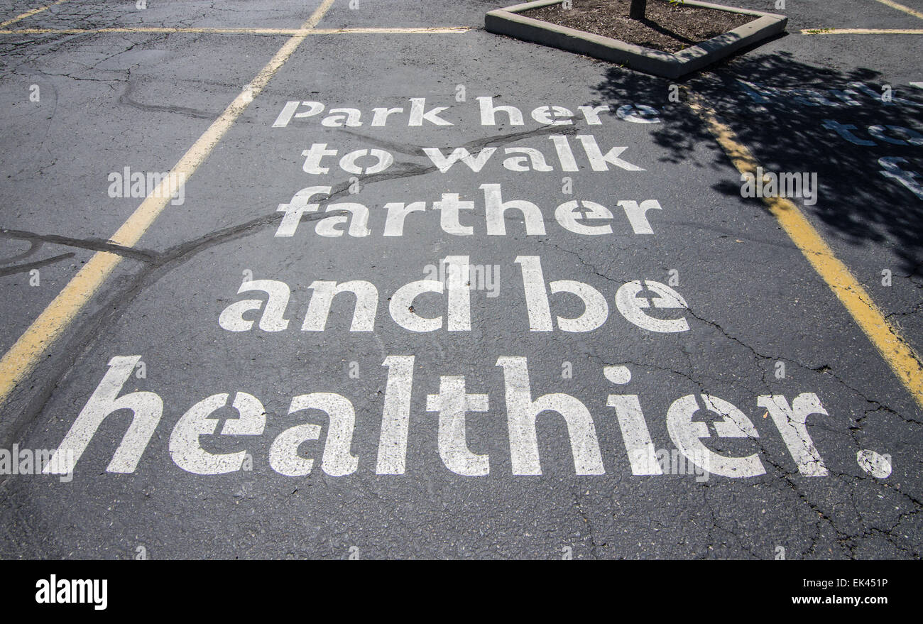 Parcheggiare qui a camminare più lontano e più sano. Un parcheggio segno ad un negozio di alimentari la promozione di esercizio e di una migliore salute. Foto Stock