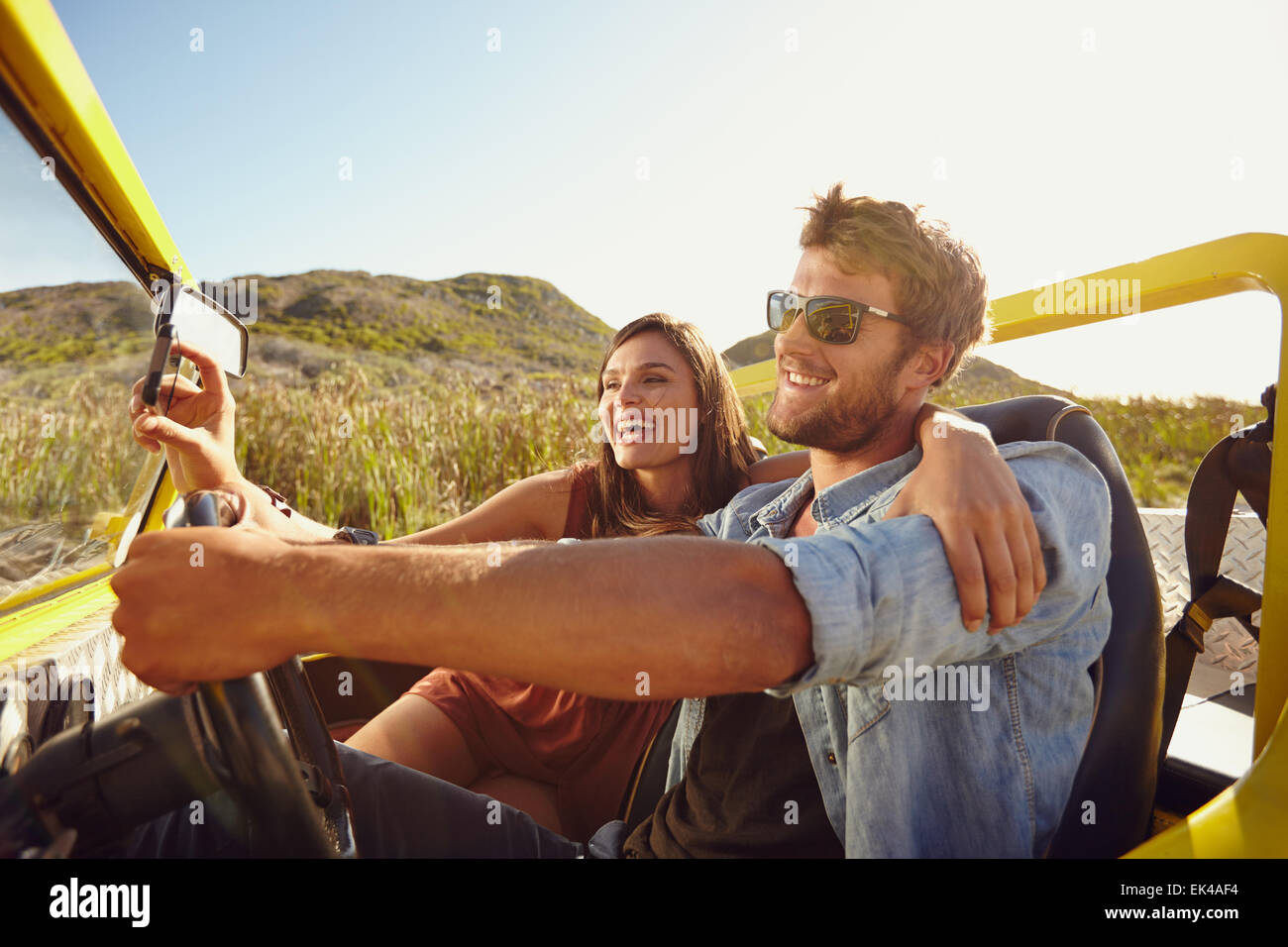 Uomo alla guida di un buggy sulla spiaggia con la donna prendendo selfie sul suo smart phone. Giovane divertirsi sul viaggio in un giorno d'estate. Foto Stock