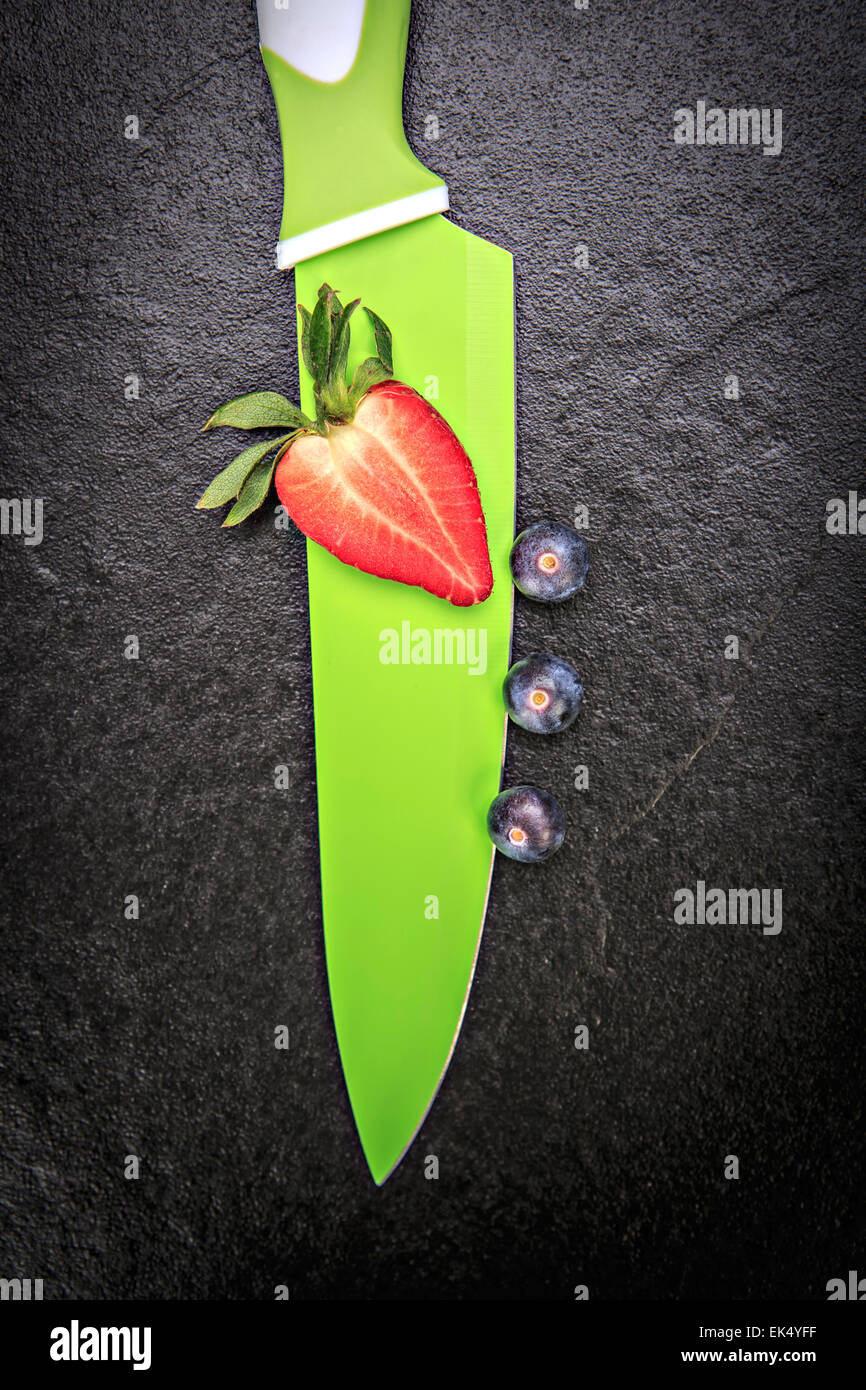 Coltello da cucina con lamponi e fragole su una lastra di pietra Foto Stock