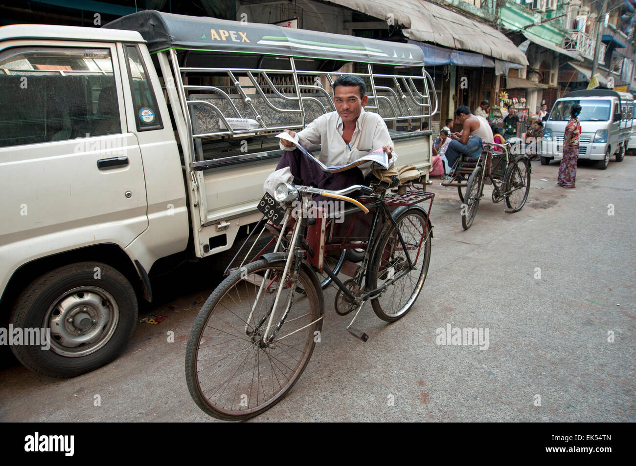 Felice di birmani rickshaw driver cerca dal suo giornale seduto su un rickshaw taxi Yangon Myanmar Foto Stock