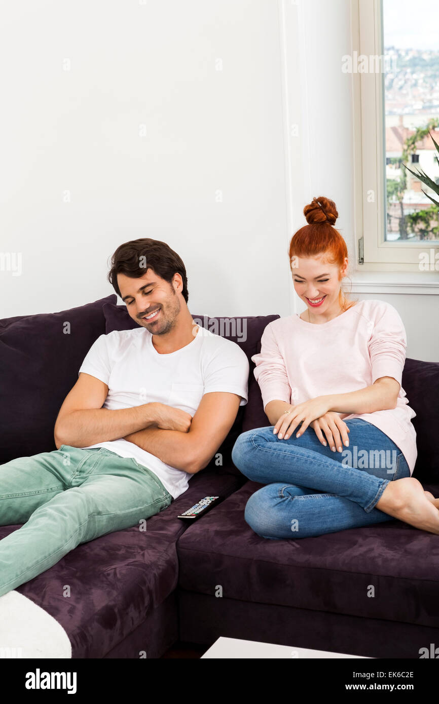 Felice giovane coppia dolce in abbigliamento Casual sorridente ad ogni altro mentre è seduta sul divano del soggiorno Foto Stock