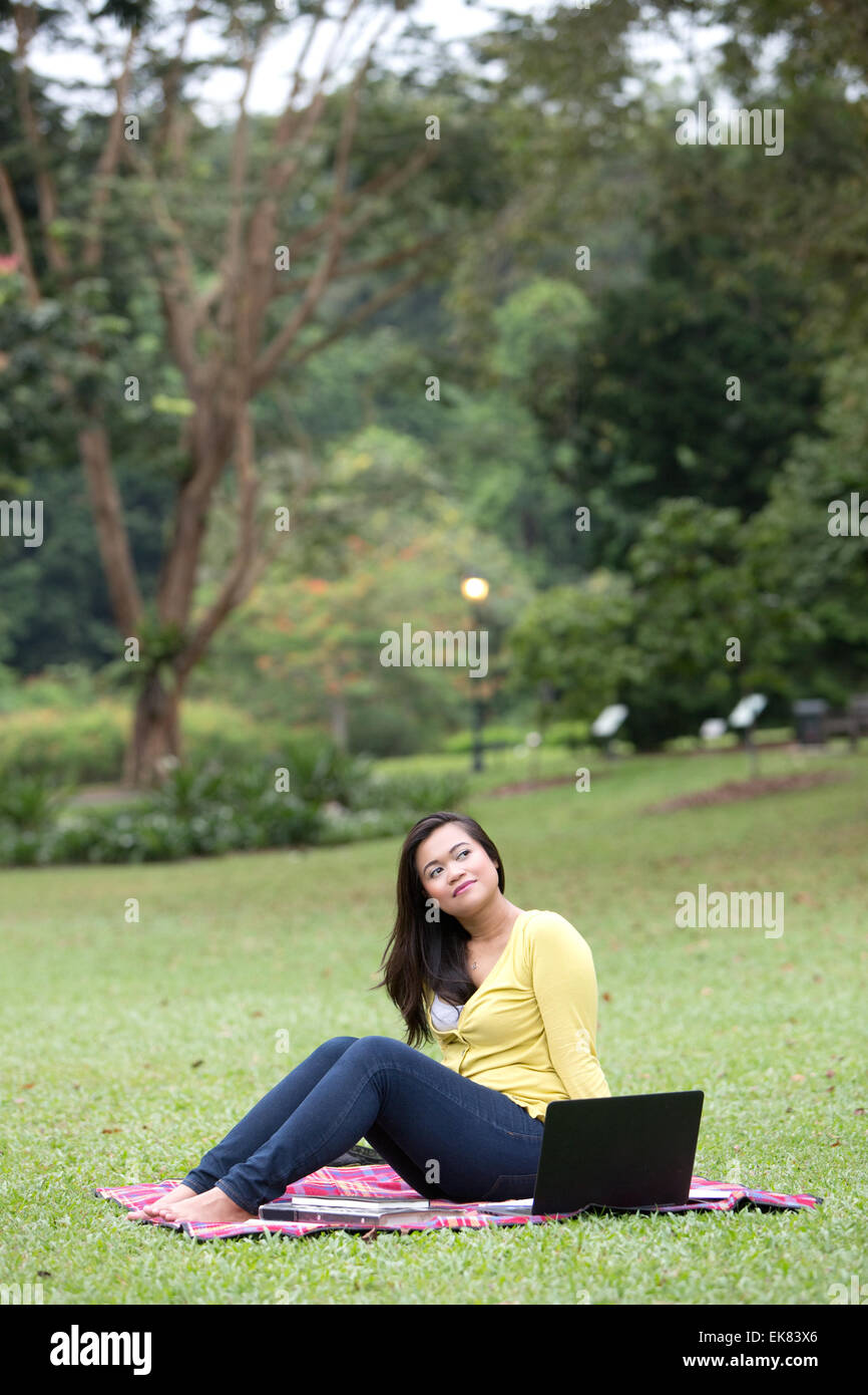 Bella giovane femmina università o college studente riflessivo, con libri e computer portatile, seduto in un parco. Foto Stock