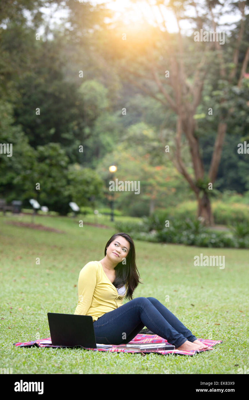 Bella giovane femmina università o college studente riflessivo, con libri e computer portatile, seduto in un parco. Foto Stock