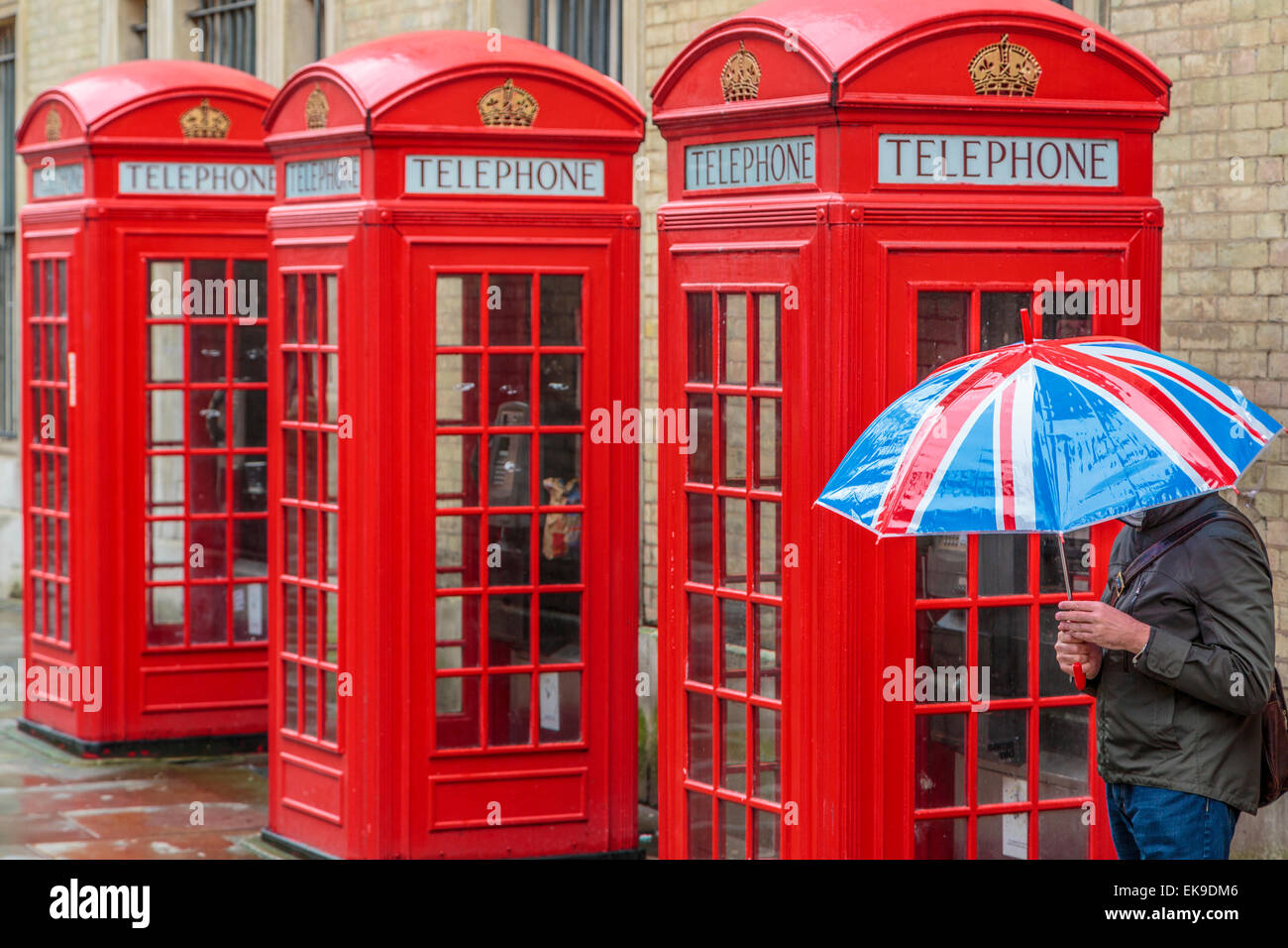 Red London cabine telefoniche sotto la pioggia con una persona in possesso di una Unione Jack ombrello, Londra Inghilterra REGNO UNITO Foto Stock