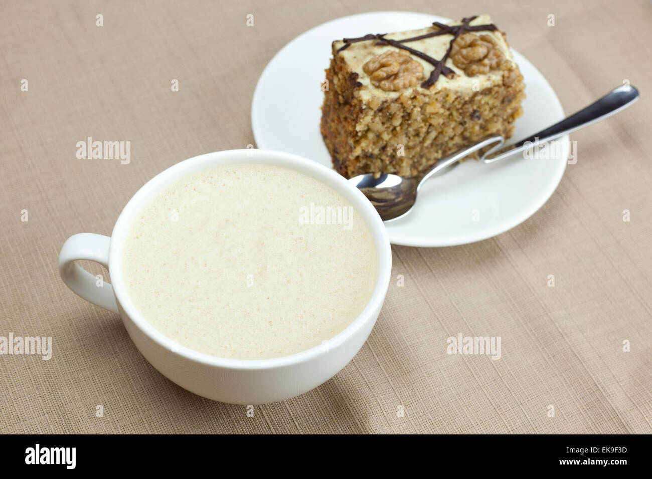 Una tazza di cappuccino, un pezzo di torta con dadi e cucchiaio giacente o Foto Stock