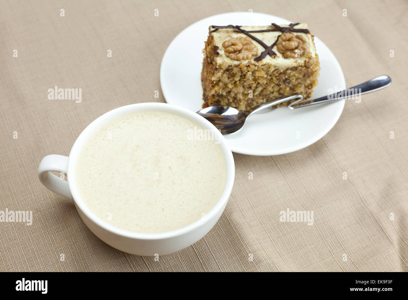 Una tazza di cappuccino, un pezzo di torta con dadi e cucchiaio giacente o Foto Stock