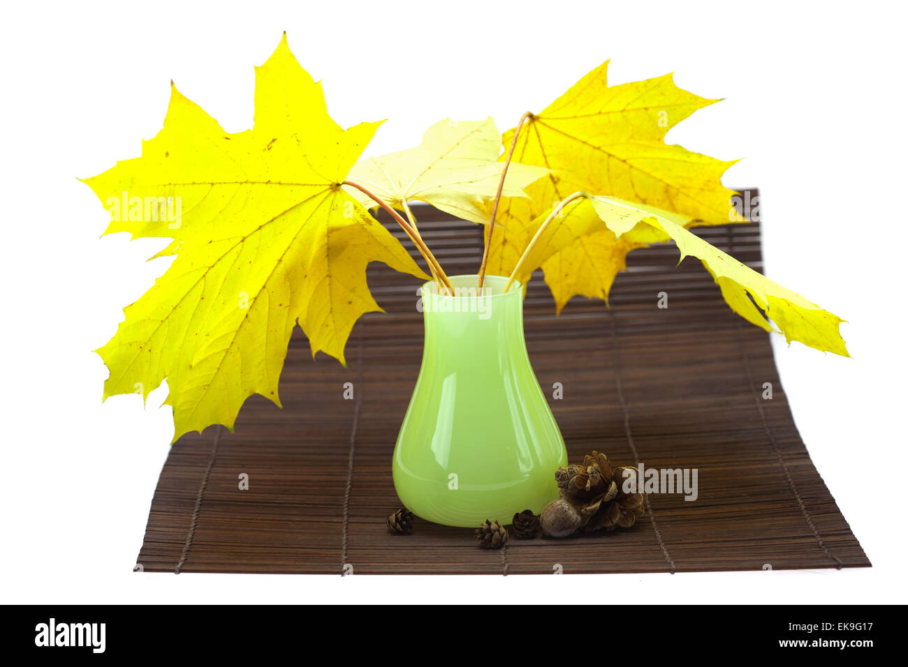 Giallo di foglie di acero e gemme in un vaso su una stuoia di bambù Foto Stock