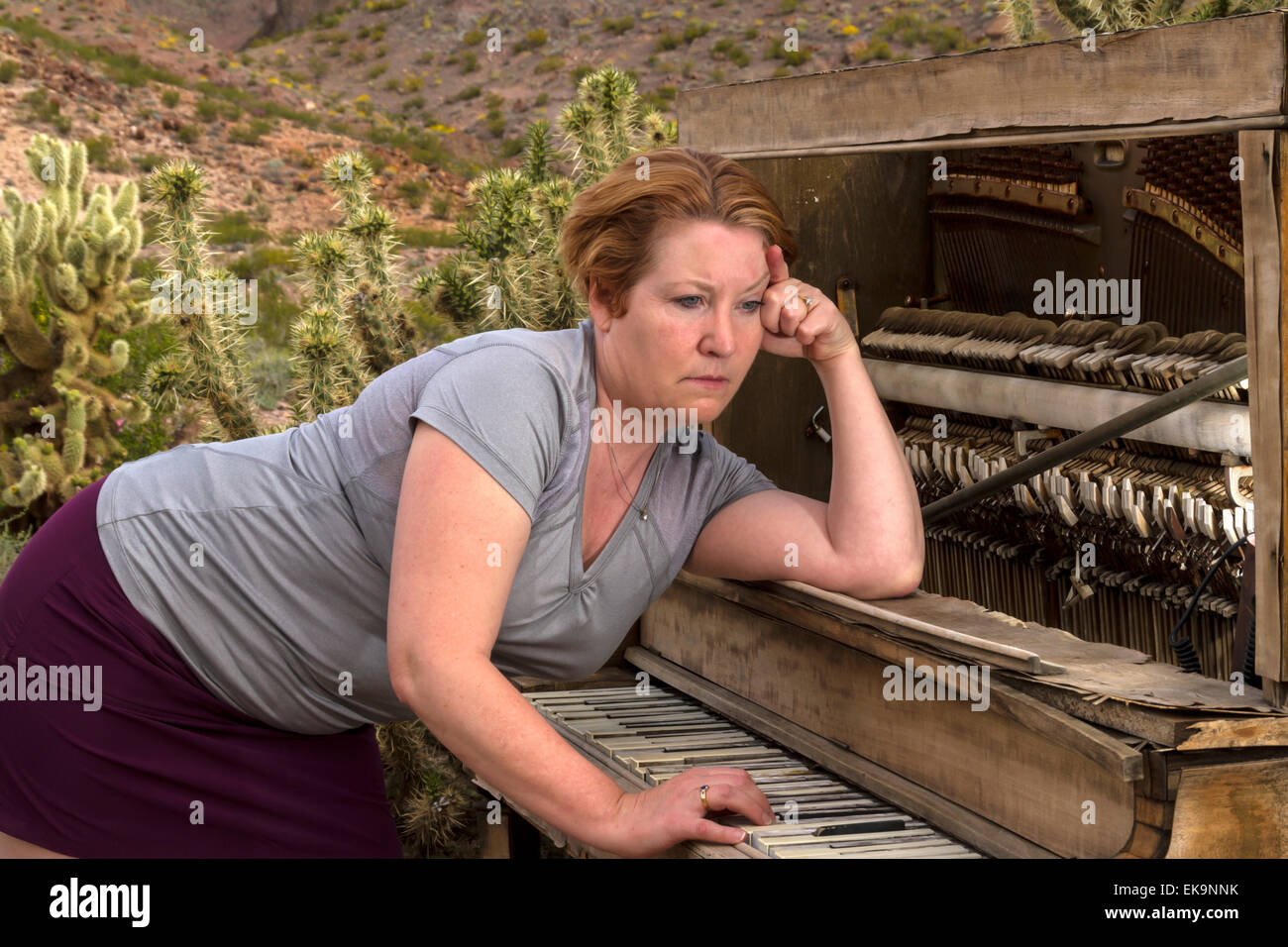 Donna matura nel deserto impostazione riproduzione di un legno antico pianoforte con un triste, espressione contemplativa Foto Stock