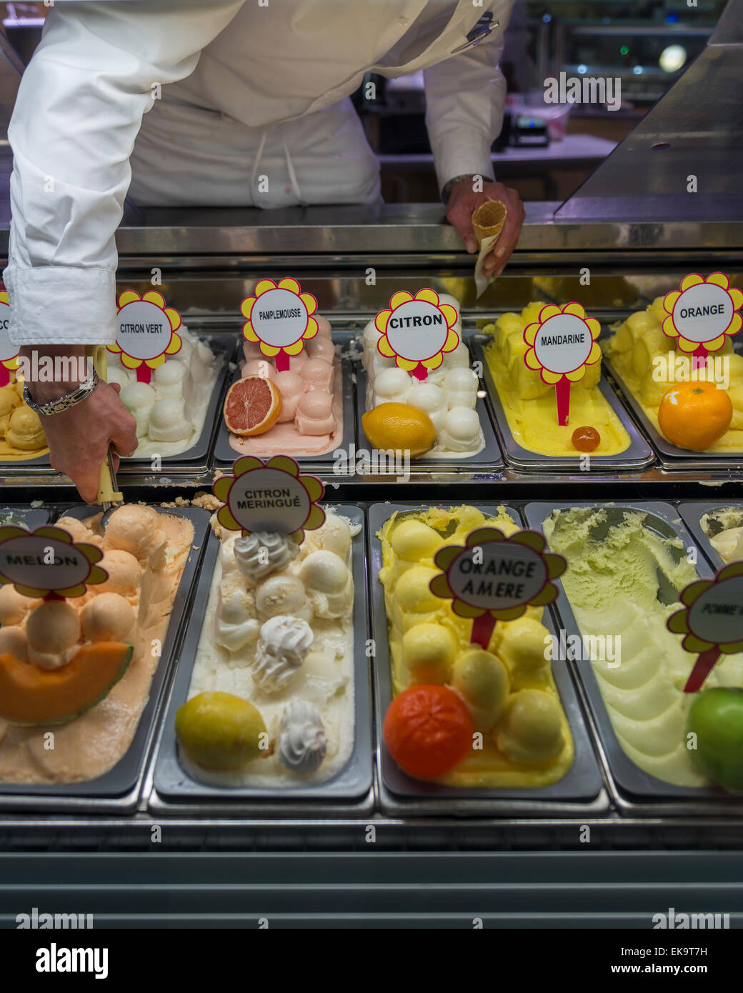 Un display di ghiaccio aromatizzato creme in un congelatore con un uomo prendendo un convogliatore per un cono Foto Stock