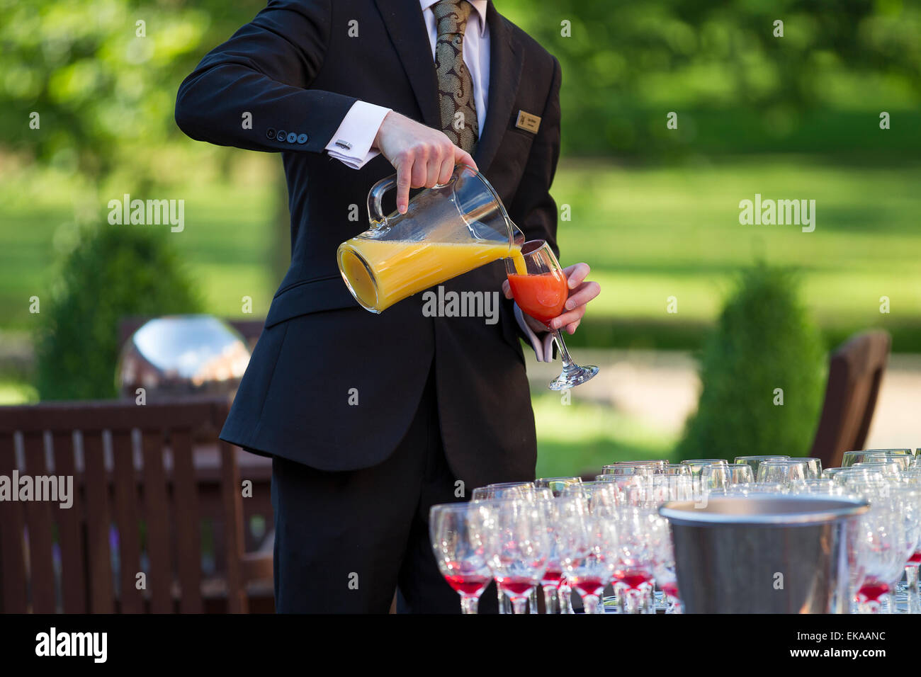 Un cameriere serve un analcolico cocktail di frutta che indossa una tuta e tirante Foto Stock