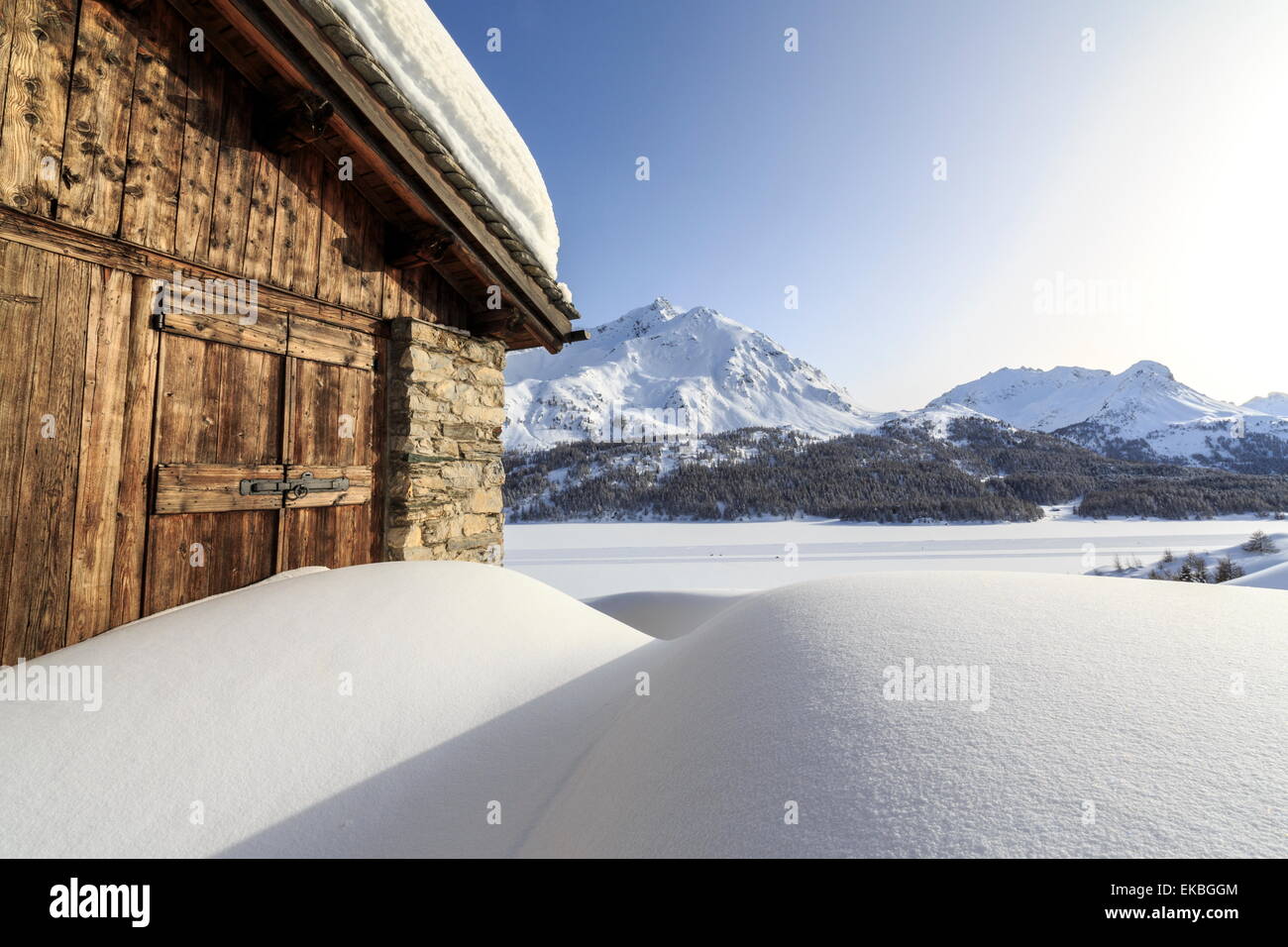 Il sole che illumina una tipica capanna ricoperta di neve presso il Passo del Maloja, Grigioni, alpi svizzere, Svizzera Foto Stock