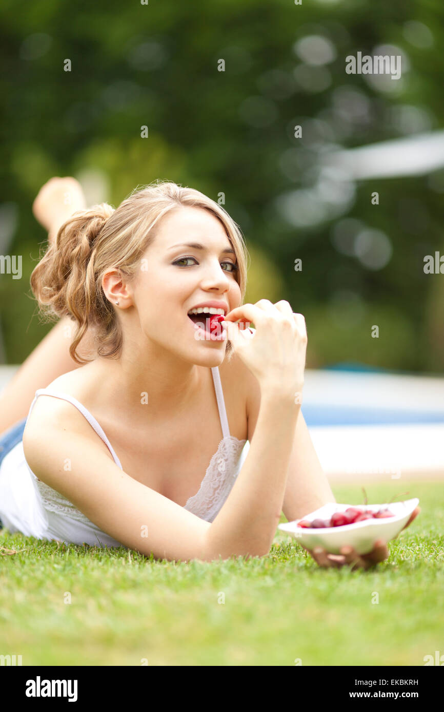 Belle donne mangiare una ciliegia sull'erba Foto Stock