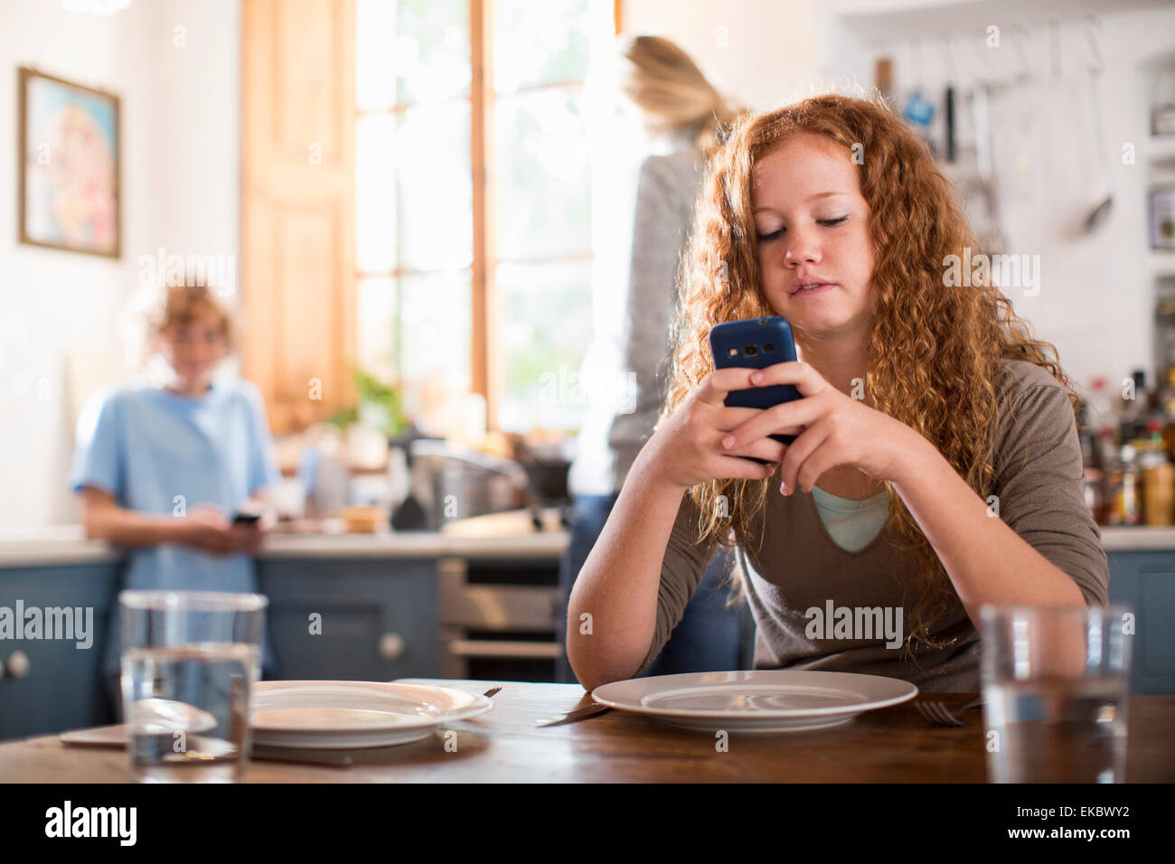 Ragazza adolescente utilizza lo smartphone al tavolo da pranzo Foto Stock