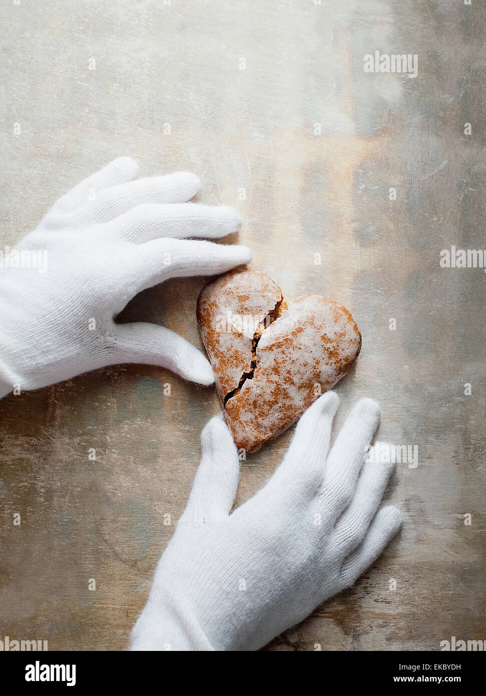 Mani guantate tenendo a forma di cuore gingerbread cookie Foto Stock