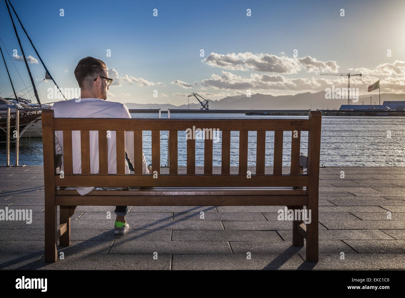 Giovane uomo rilassante su banco dal porto di Cagliari, Sardegna, Italia Foto Stock