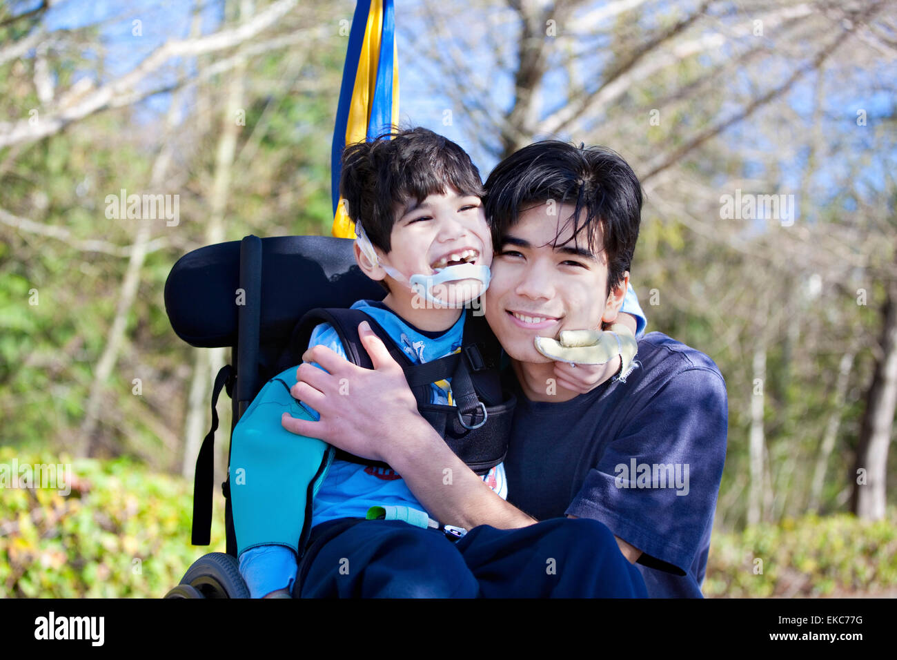Little Boy disabili in carrozzella abbracciando il fratello maggiore all'aperto Foto Stock