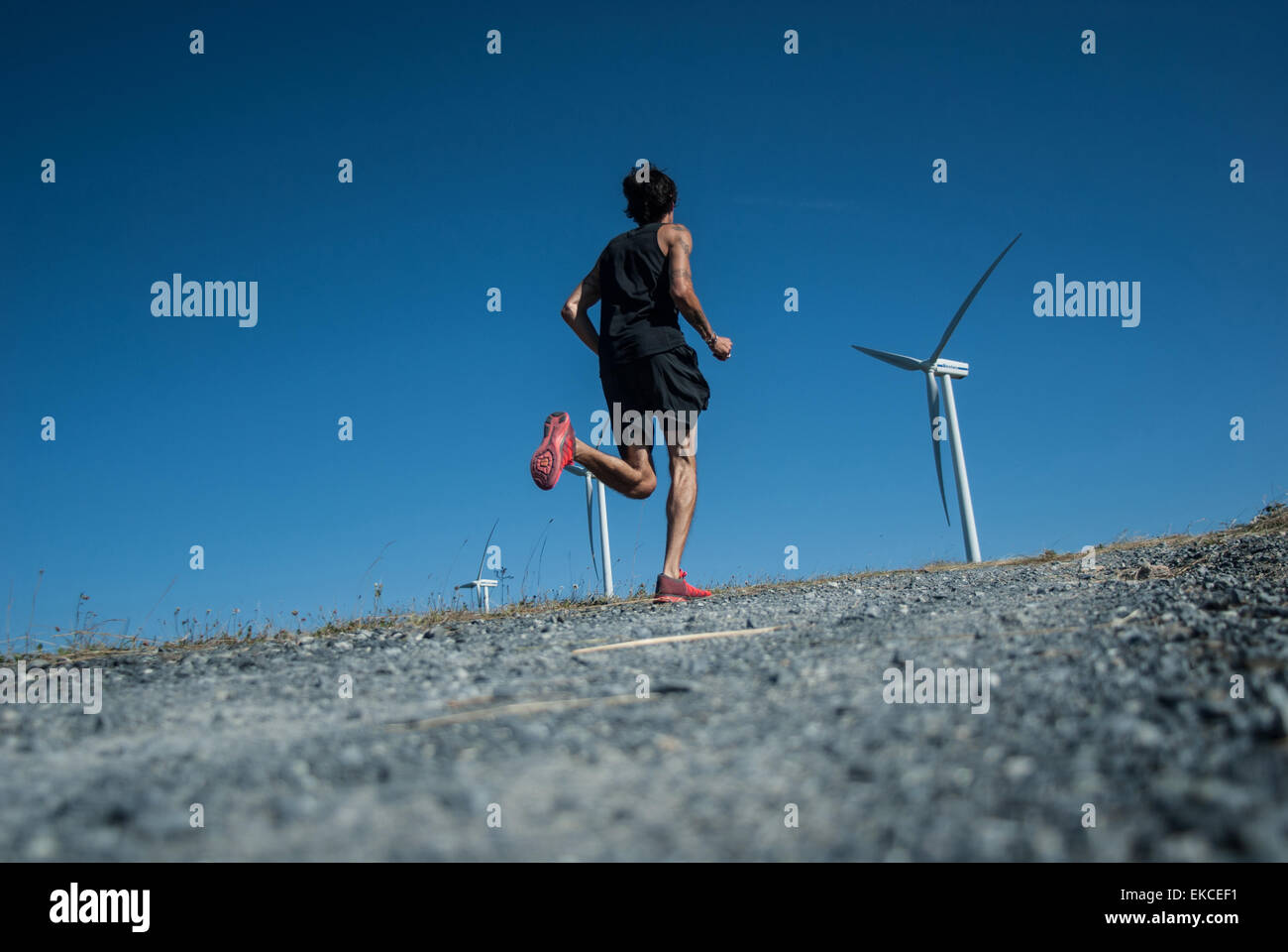 Metà uomo adulto jogging fino alla cima di una collina verso le turbine eoliche Foto Stock