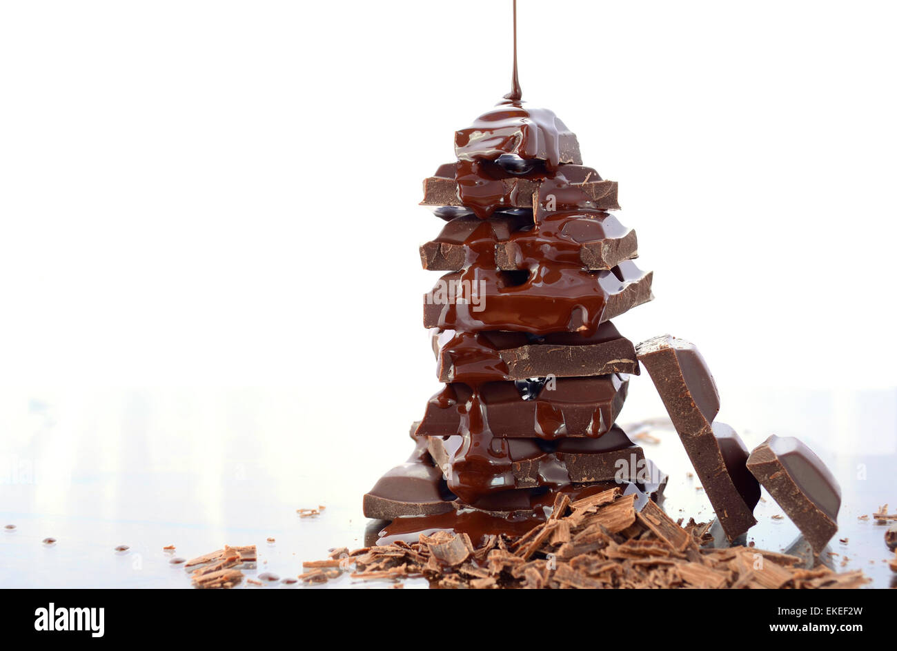 Pila di cioccolato con colata di cioccolato in salsa di vetro riflettente contro uno sfondo bianco. Foto Stock