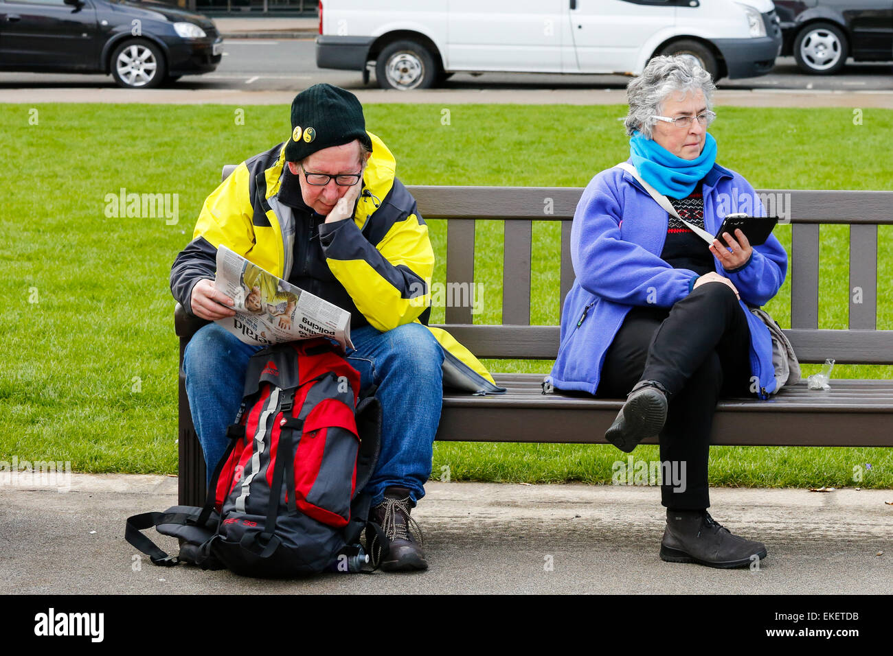 L uomo e la donna seduta sulle panchine pubbliche nel centro della città di Glasgow, una lettura di un quotidiano, l'altra lettura il suo telefono, Glasgow Foto Stock