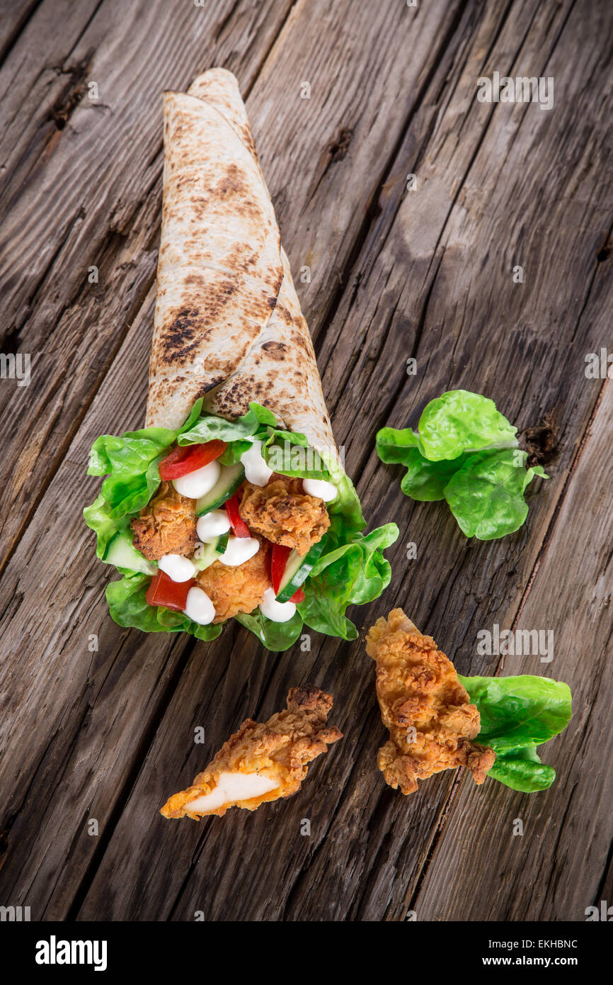 Le strisce di pollo in una Tortilla avvolgere con lattuga su legno. Foto Stock