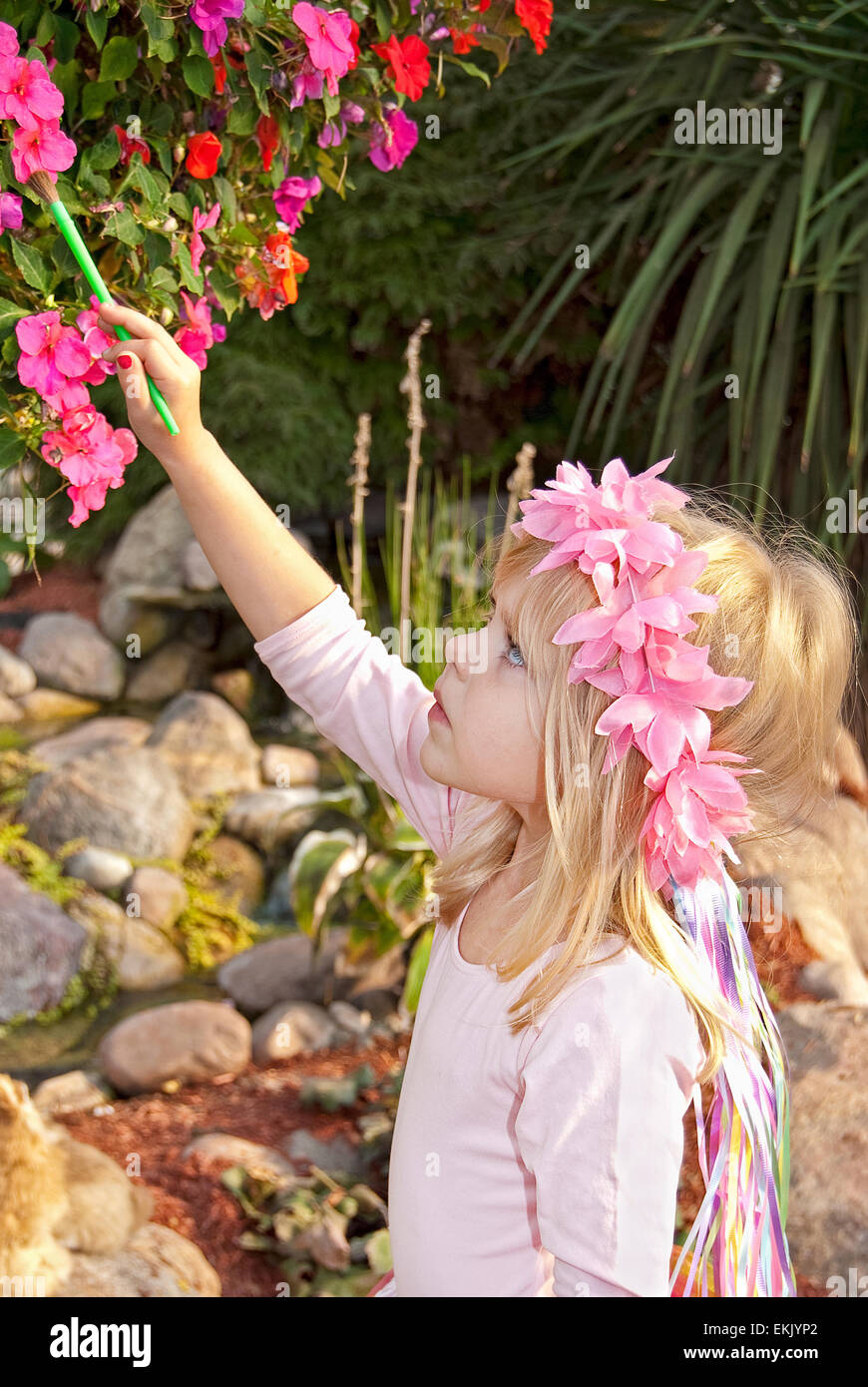 Piccola ragazza caucasica con motivi floreali di alloro e di verniciatura di un fiore rosa in giardino. Foto Stock