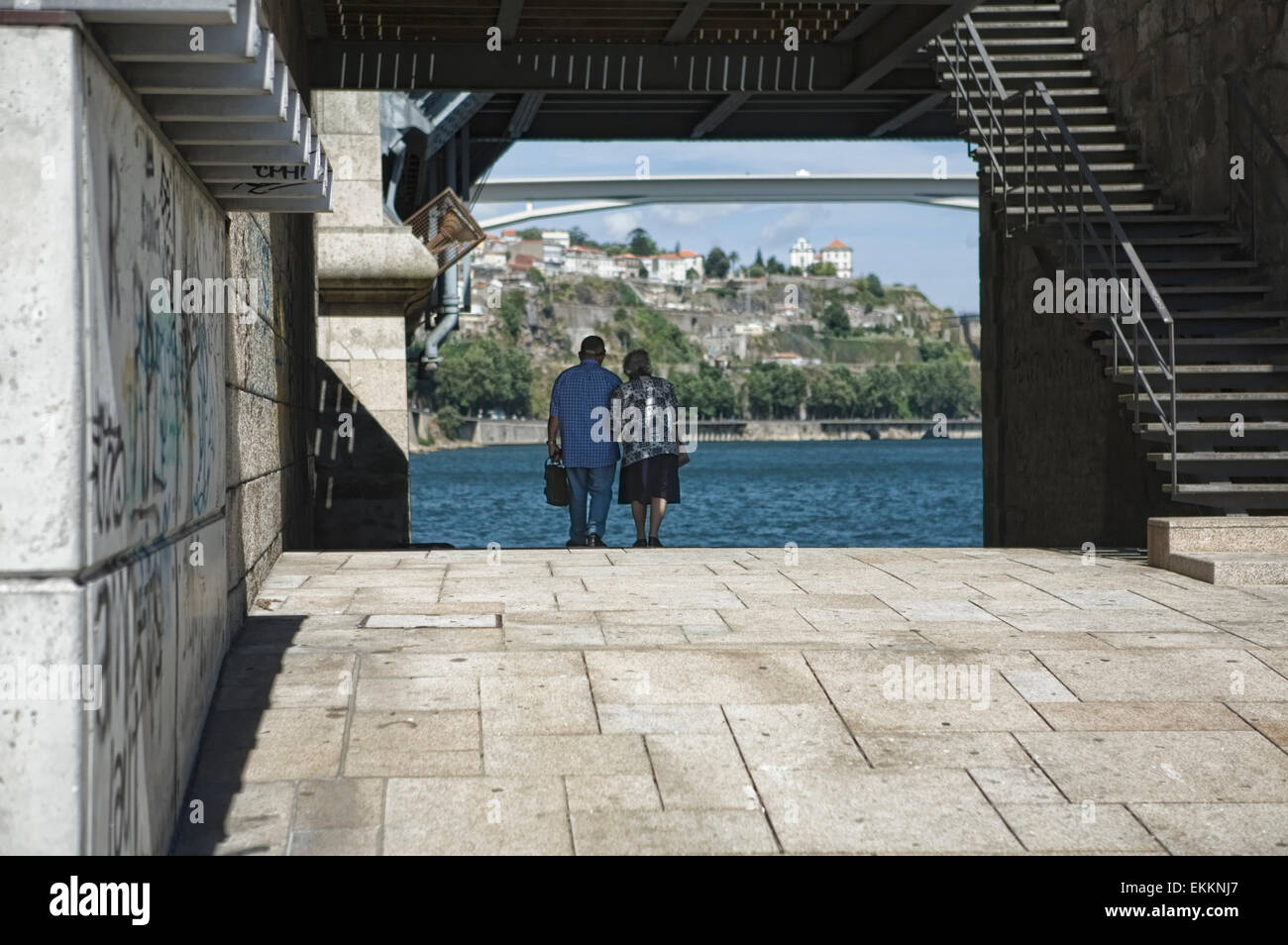 Un vecchio paio di camminare mano nella mano sotto il ponte di ferro di Oporto, Portogallo Foto Stock