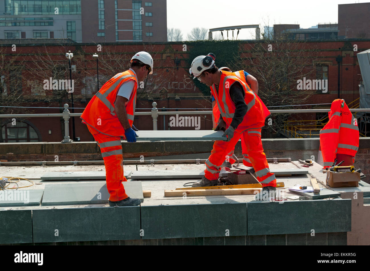 Lavoratori ponendo una lastra di pietra sulla nuova piattaforma del Deansgate-Castlefield Metrolink fermata del tram, Manchester, Inghilterra, Regno Unito Foto Stock