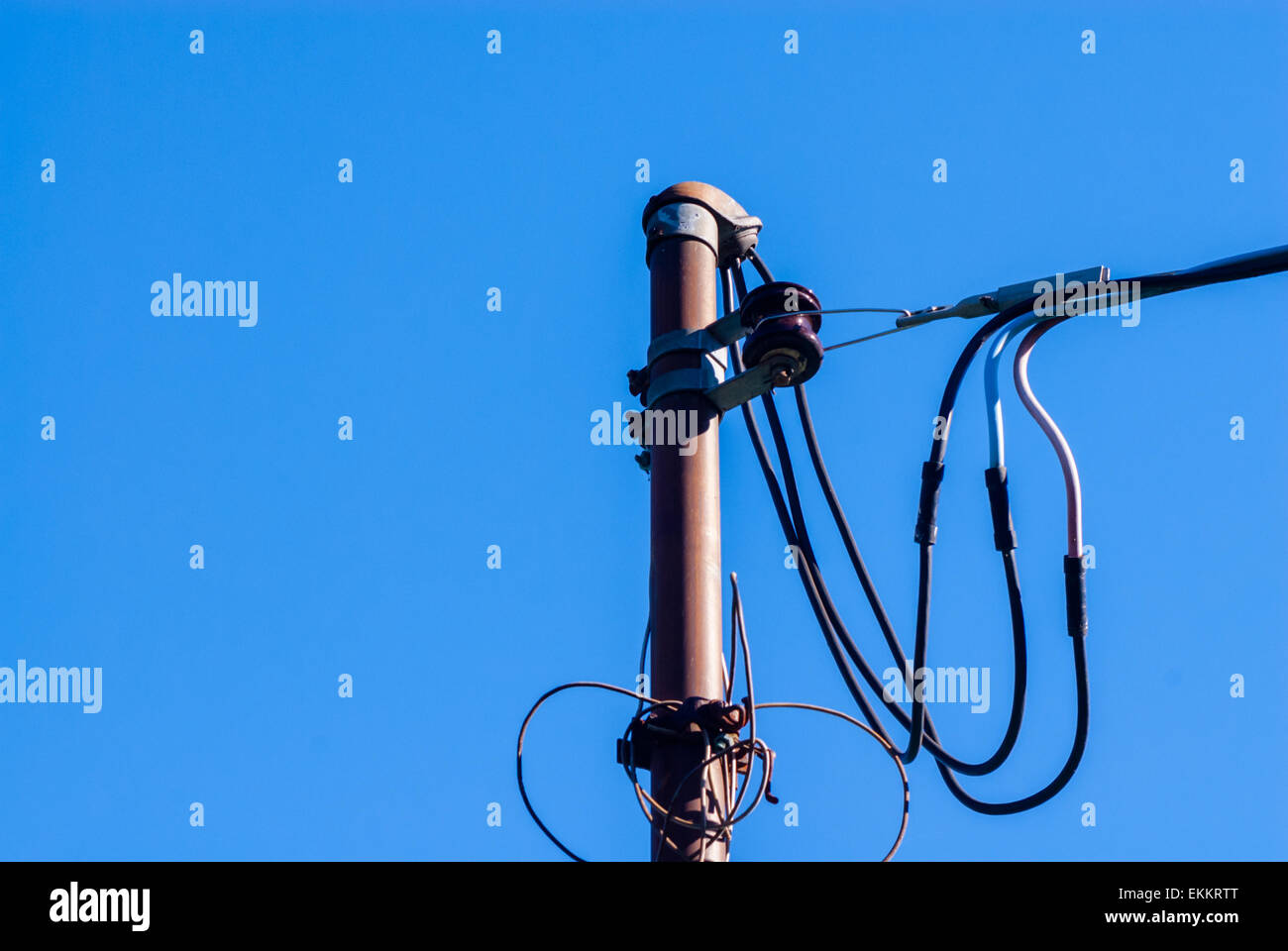 I cavi di alimentazione e i collegamenti sul palo metallico contro il cielo blu e chiaro. Foto Stock